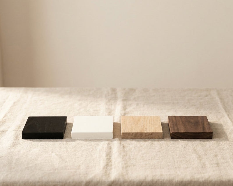 Four timber samples in a row on linen: black stained, white painted, natural oak and dark walnut