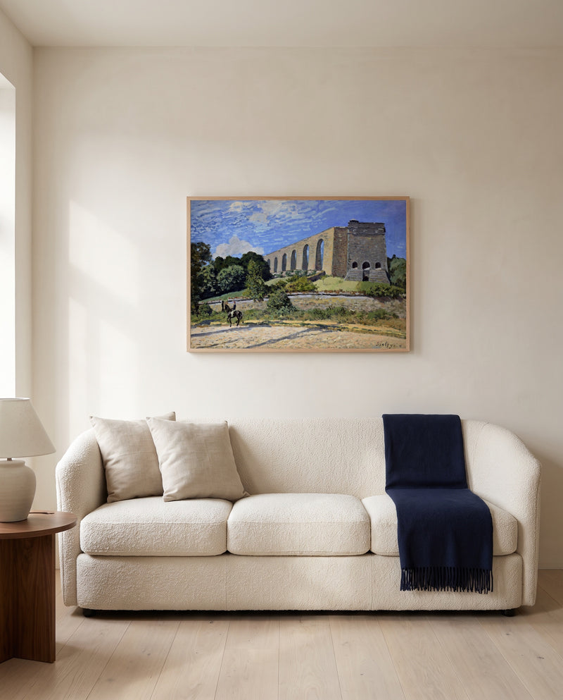 The Aqueduct at Marly by Alfred Sisley framed in natural oak above a cream sofa in a warm living room