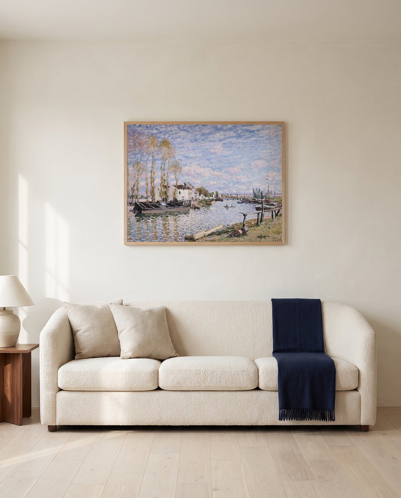 Loing at Saint-Mammès by Alfred Sisley framed in natural oak above a cream sofa in a warm living room