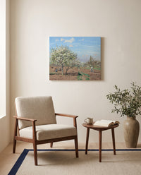 Orchard in Bloom by Camille Pissarro as a stretched canvas above a linen lounge chair in a reading corner