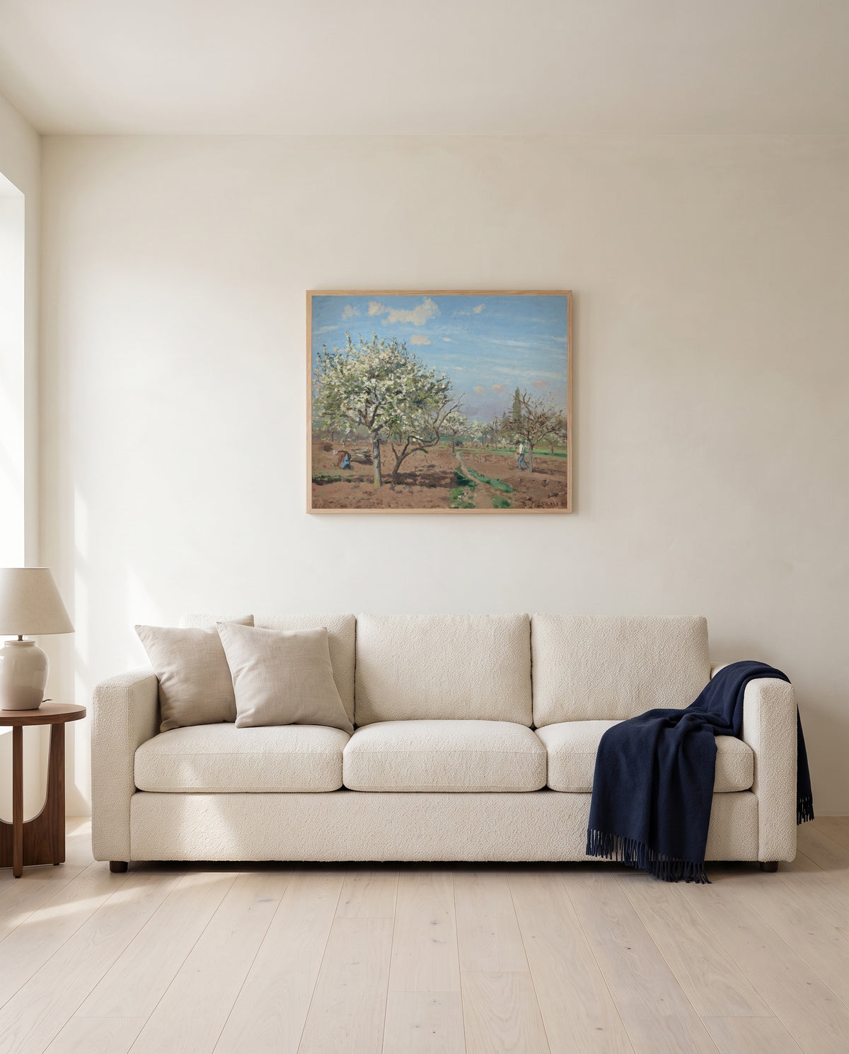 Orchard in Bloom by Camille Pissarro framed in natural oak above a cream sofa in a warm living room