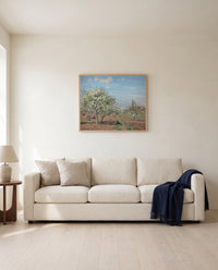 Orchard in Bloom by Camille Pissarro framed in natural oak above a cream sofa in a warm living room