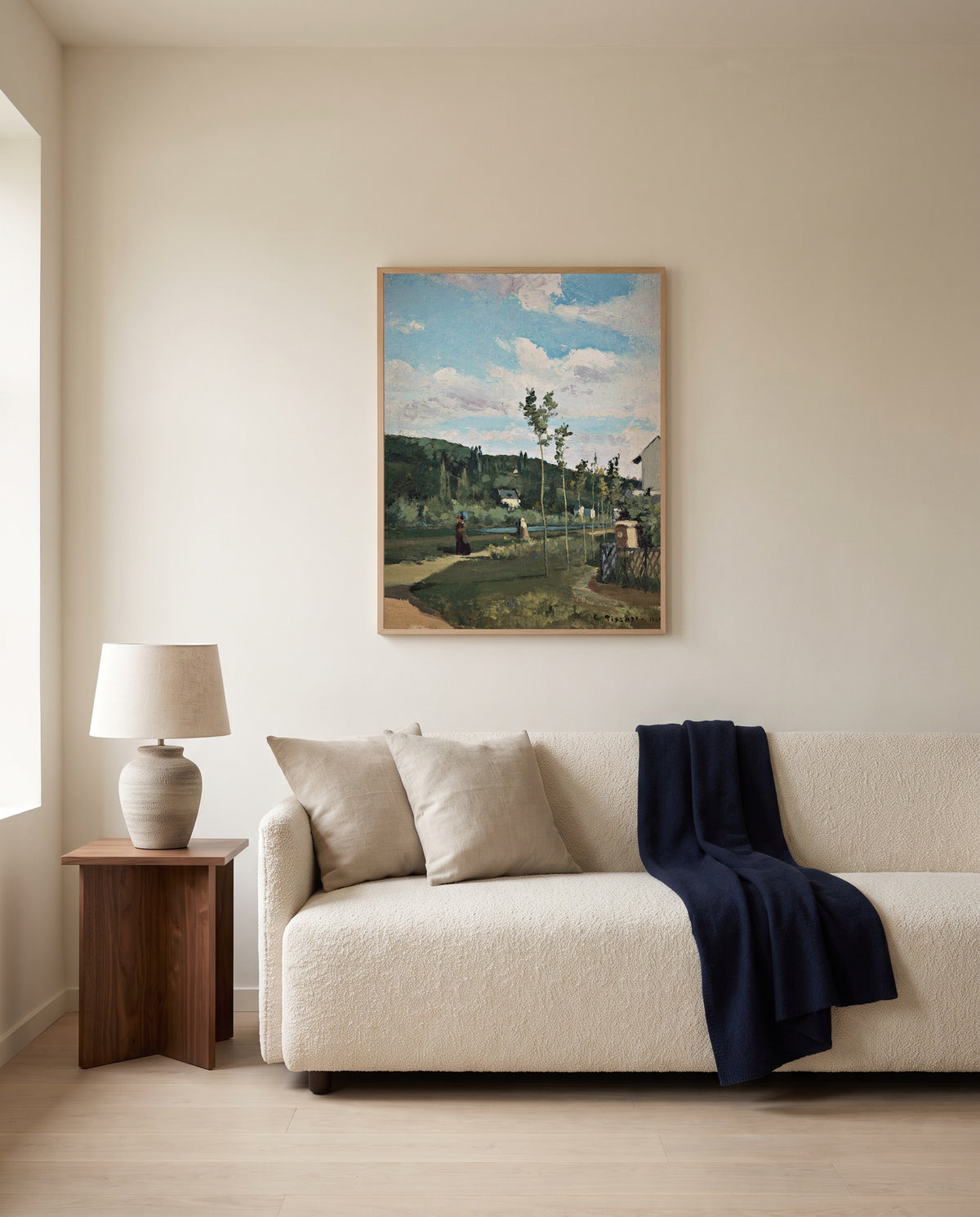 Strollers on a Country Road by Camille Pissarro framed in natural oak above a cream sofa in a warm living room