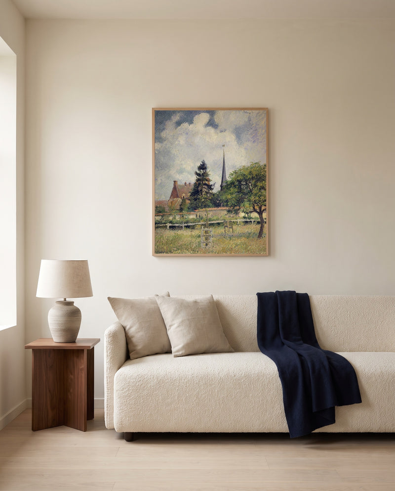 The Church at Éragny by Camille Pissarro framed in natural oak above a cream sofa in a warm living room