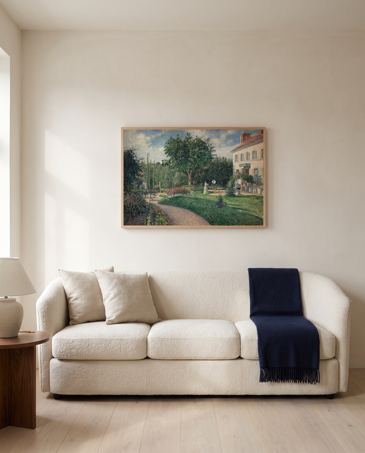 Garden of Les Mathurins by Camille Pissarro framed in natural oak above a cream sofa in a warm living room