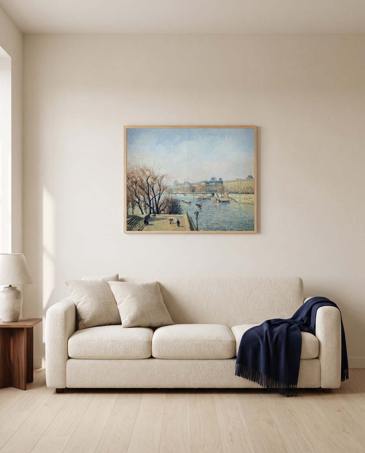 The Louvre, Morning by Camille Pissarro framed in natural oak above a cream sofa in a warm living room