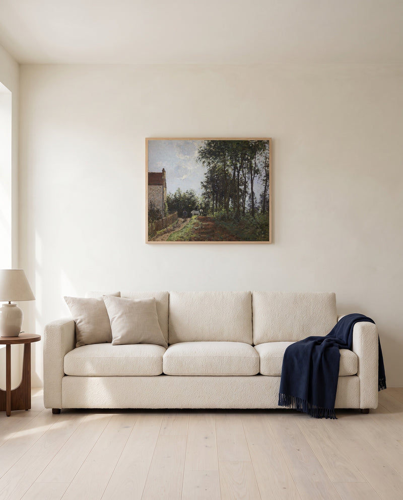 The Road Near the Farm by Camille Pissarro framed in natural oak above a cream sofa in a warm living room
