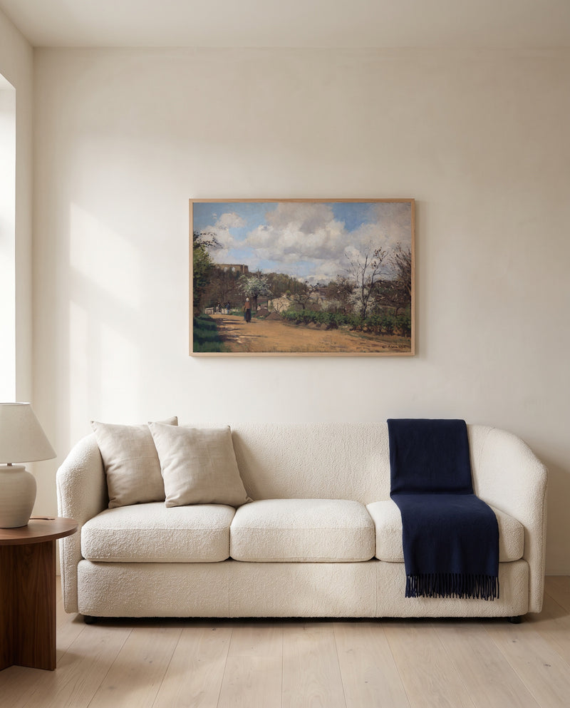 View from Louveciennes by Camille Pissarro framed in natural oak above a cream sofa in a warm living room