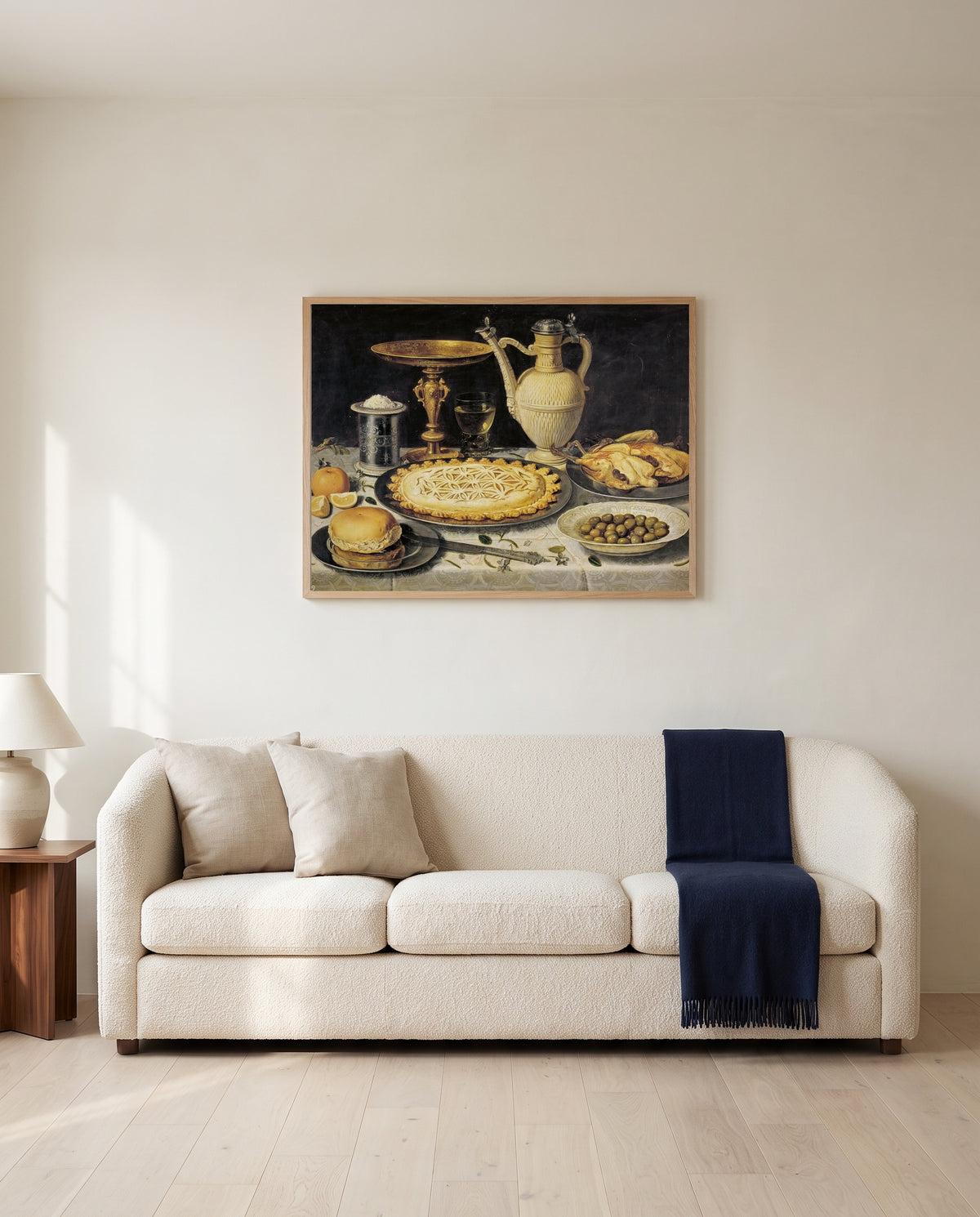 Tazza, Jug and Pie by Clara Peeters framed in natural oak above a cream sofa in a warm living room