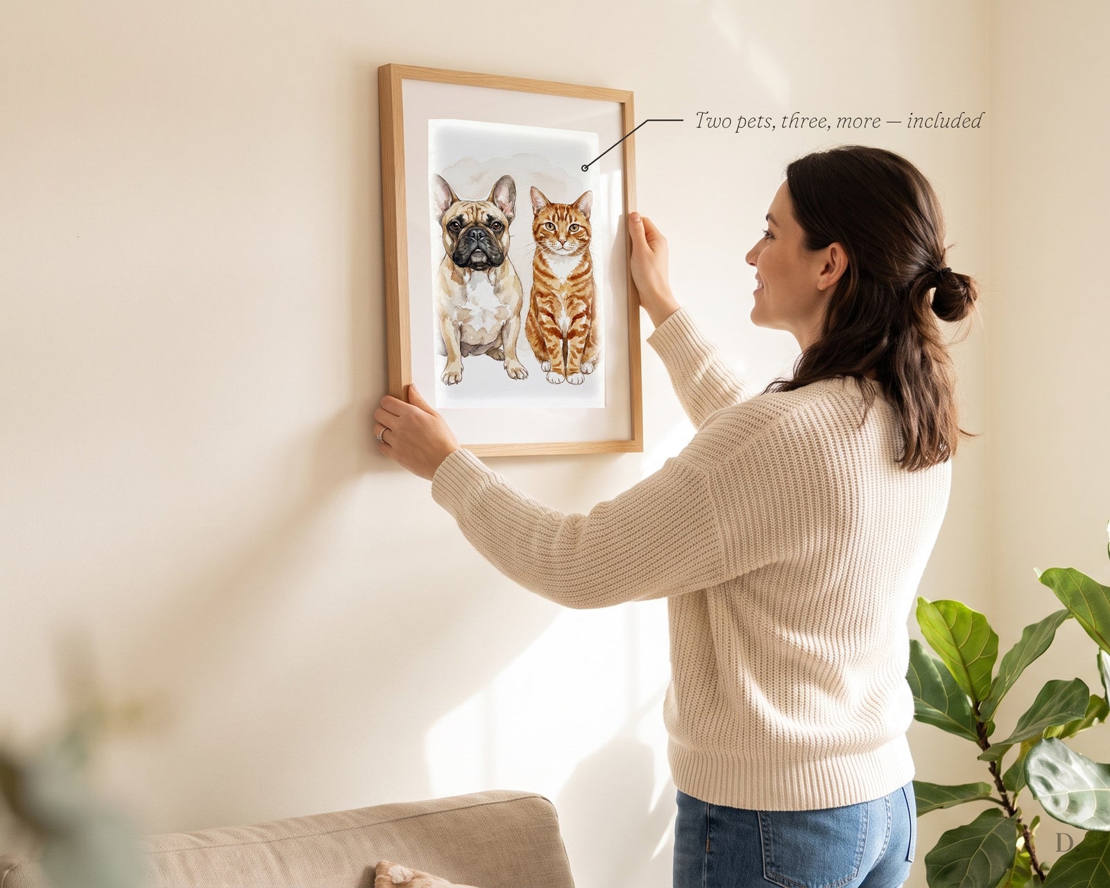 Woman hanging a framed watercolor portrait of two pets, a French bulldog and an orange tabby
