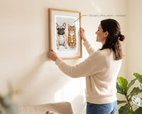 Woman hanging a framed watercolor portrait of two pets, a French bulldog and an orange tabby