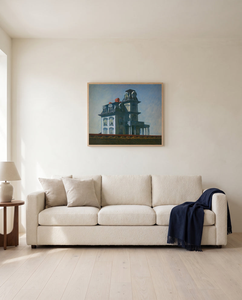 House by the Railroad by Edward Hopper framed in natural oak above a cream sofa in a warm living room