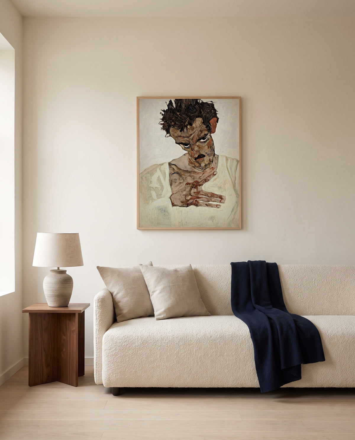 Self-Portrait, Lowered Head by Egon Schiele framed in natural oak above a cream sofa in a warm living room
