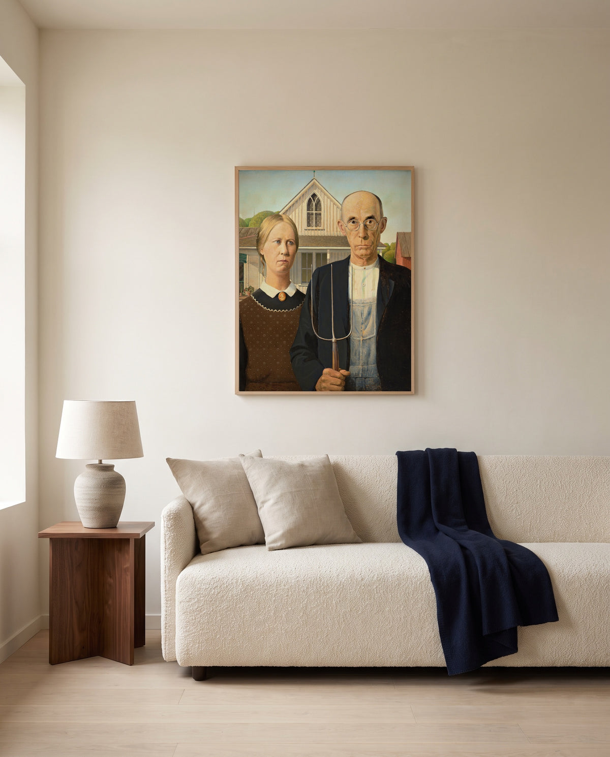 American Gothic by Grant Wood framed in natural oak above a cream sofa in a warm living room
