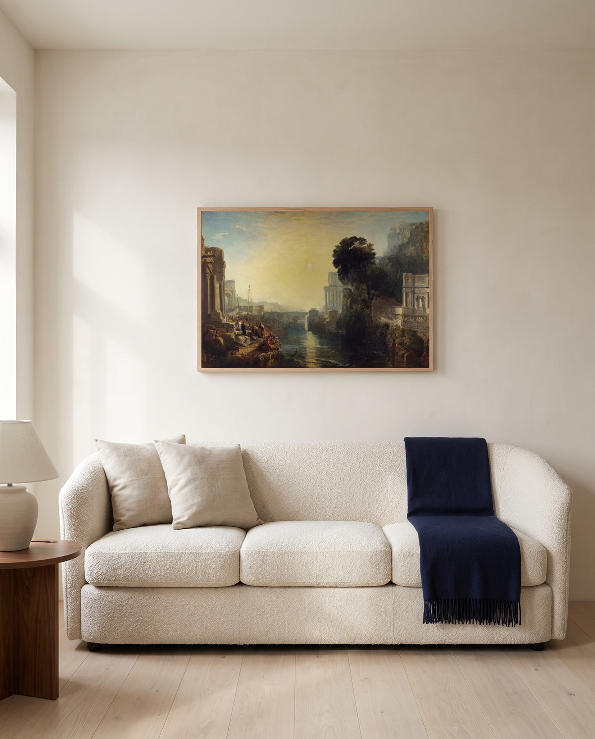 Dido building Carthage by J. M. W. Turner framed in natural oak above a cream sofa in a warm living room