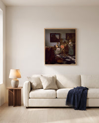 The Concert by Johannes Vermeer framed in natural oak above a cream sofa in a warm living room