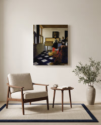 The Music Lesson by Johannes Vermeer as a stretched canvas above a linen lounge chair in a reading corner