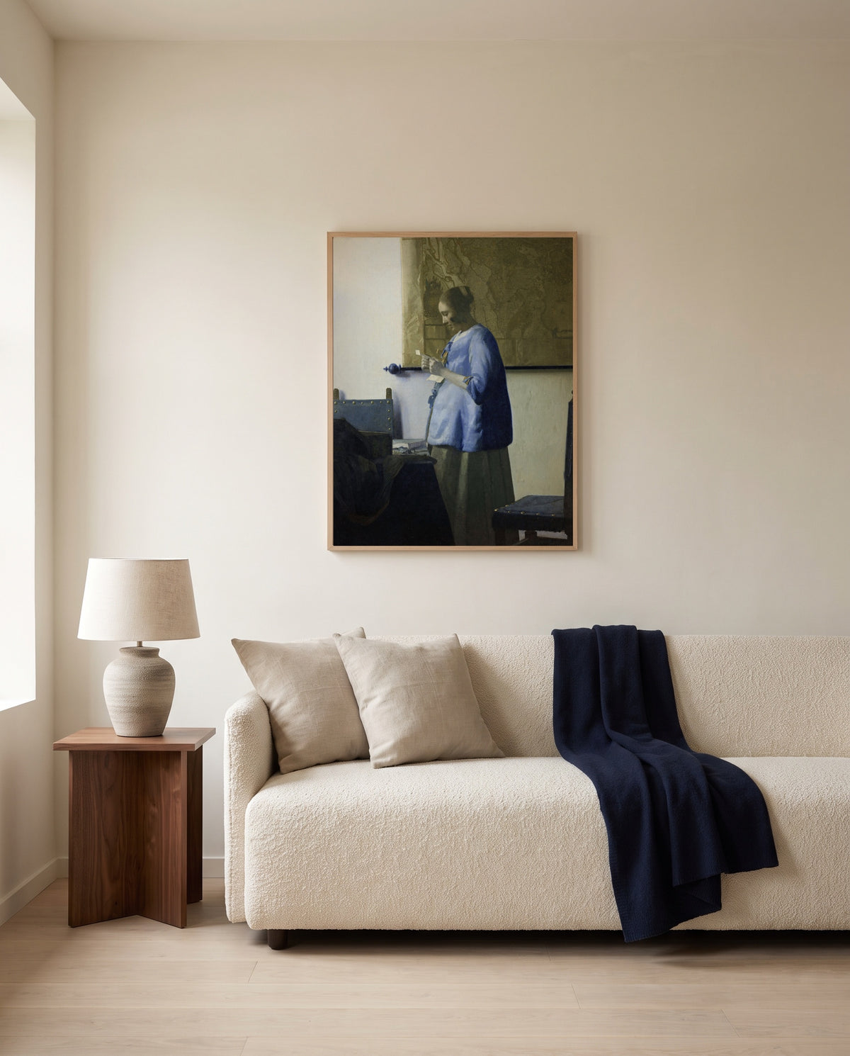 Woman in Blue Reading a Letter by Johannes Vermeer framed in natural oak above a cream sofa in a warm living room