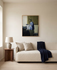 Woman in Blue Reading a Letter by Johannes Vermeer framed in natural oak above a cream sofa in a warm living room