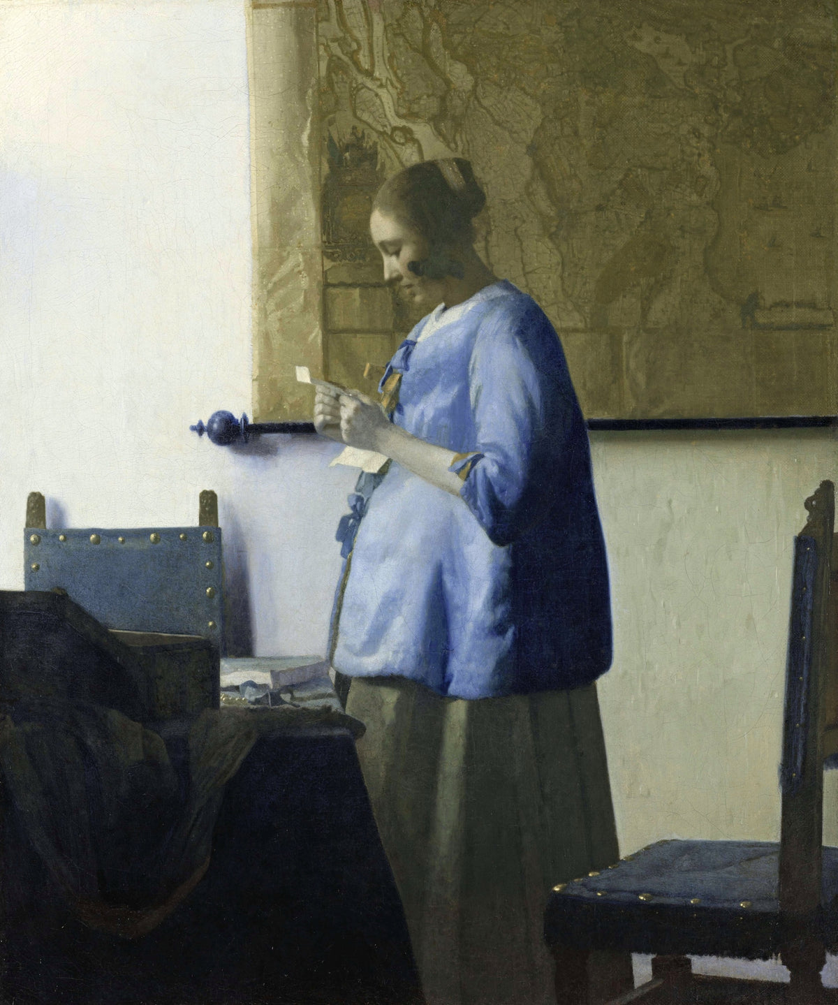 Woman in Blue Reading a Letter by Johannes Vermeer: a woman in a blue jacket reading a letter before a map on a pale wall