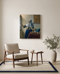 Woman with a Water Pitcher by Johannes Vermeer as a stretched canvas above a linen lounge chair in a reading corner