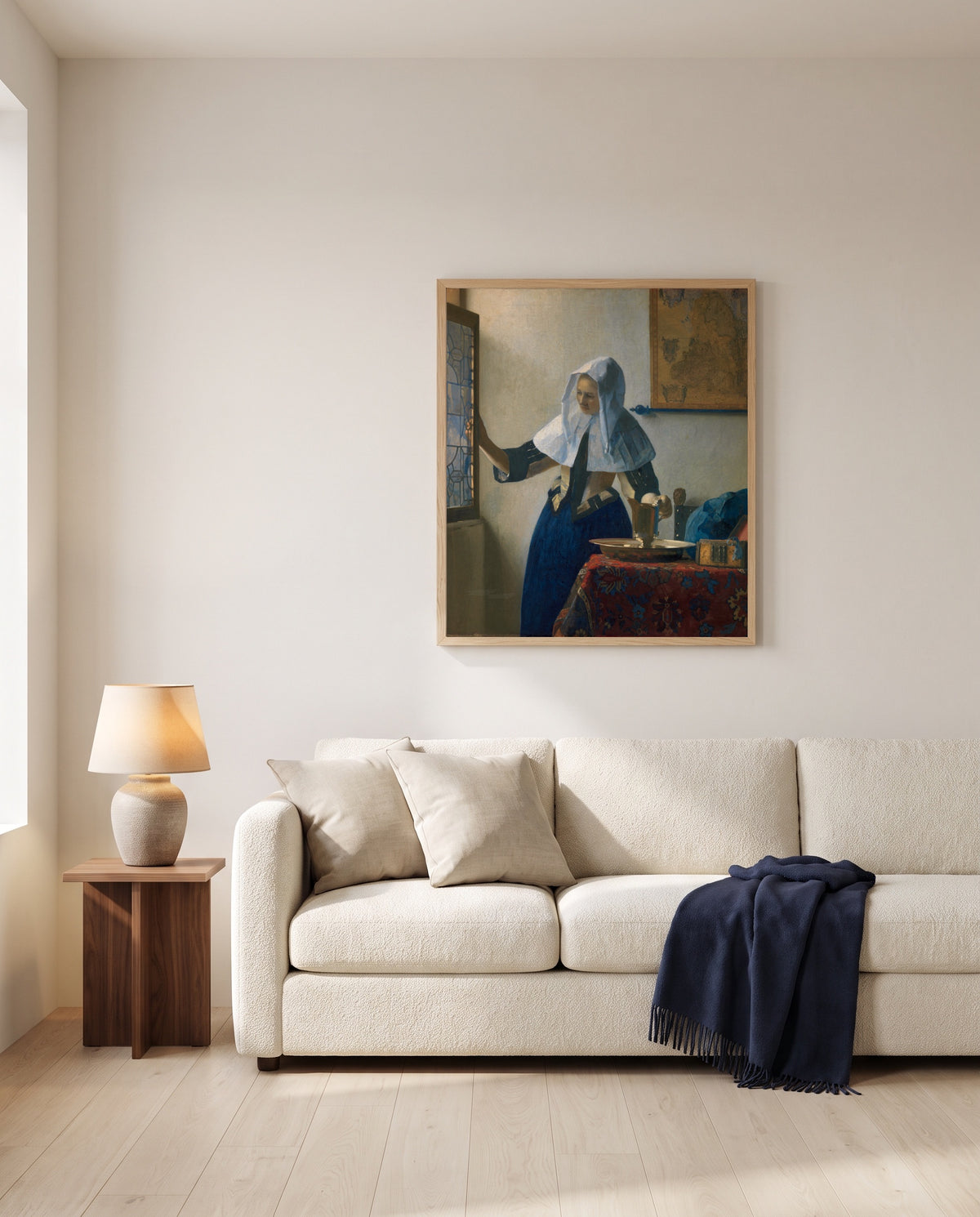Woman with a Water Pitcher by Johannes Vermeer framed in natural oak above a cream sofa in a warm living room