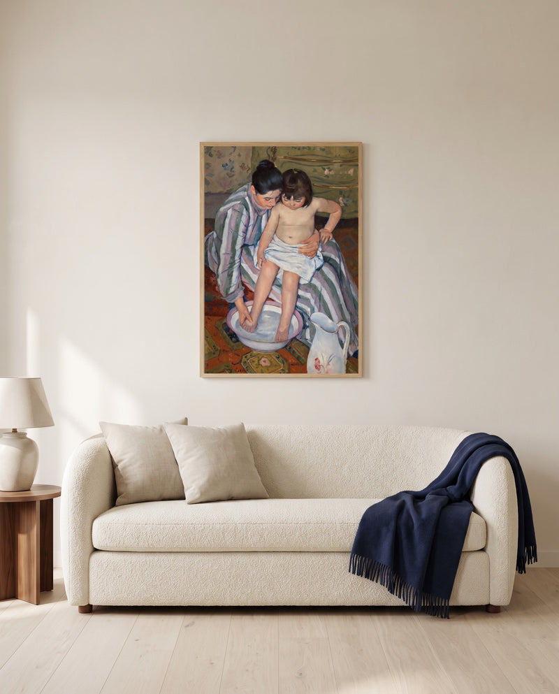 The Child’s Bath by Mary Cassatt framed in natural oak above a cream sofa in a warm living room