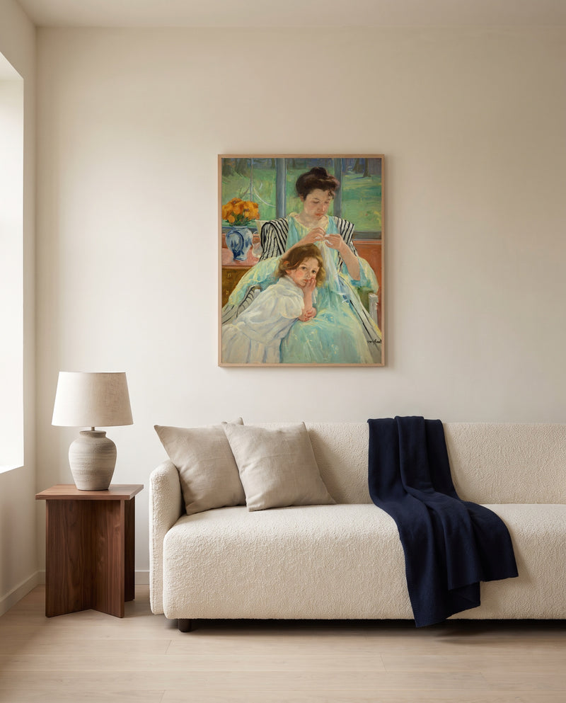 Young Mother Sewing by Mary Cassatt framed in natural oak above a cream sofa in a warm living room