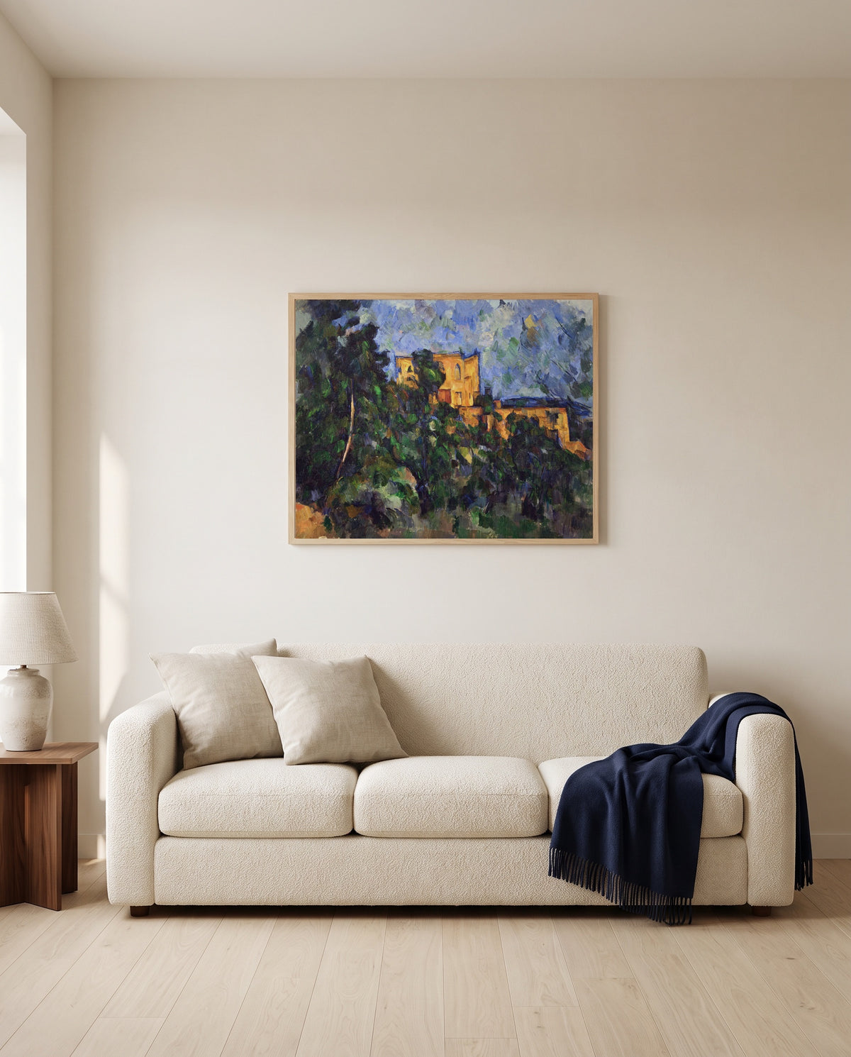 Château Noir by Paul Cézanne framed in natural oak above a cream sofa in a warm living room
