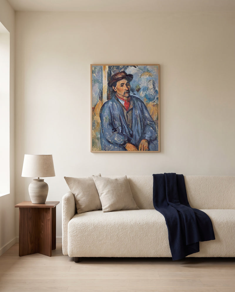 Man in a Blue Smock by Paul Cézanne framed in natural oak above a cream sofa in a warm living room