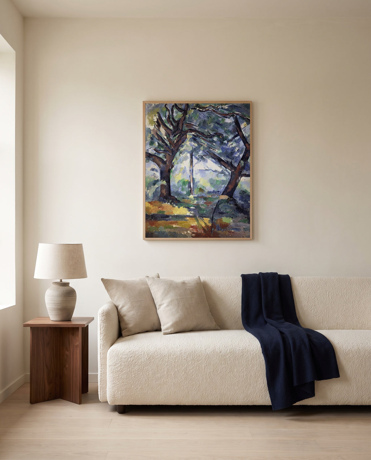 The Big Trees by Paul Cézanne framed in natural oak above a cream sofa in a warm living room