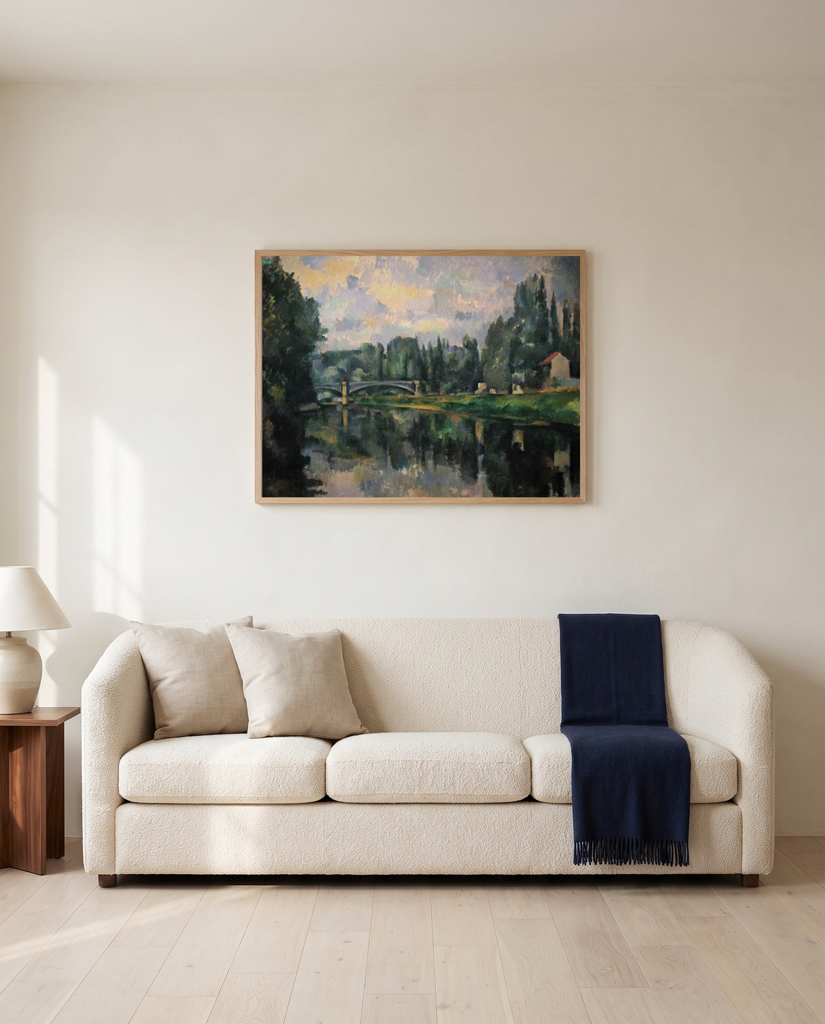 The Banks of the Marne by Paul Cézanne framed in natural oak above a cream sofa in a warm living room