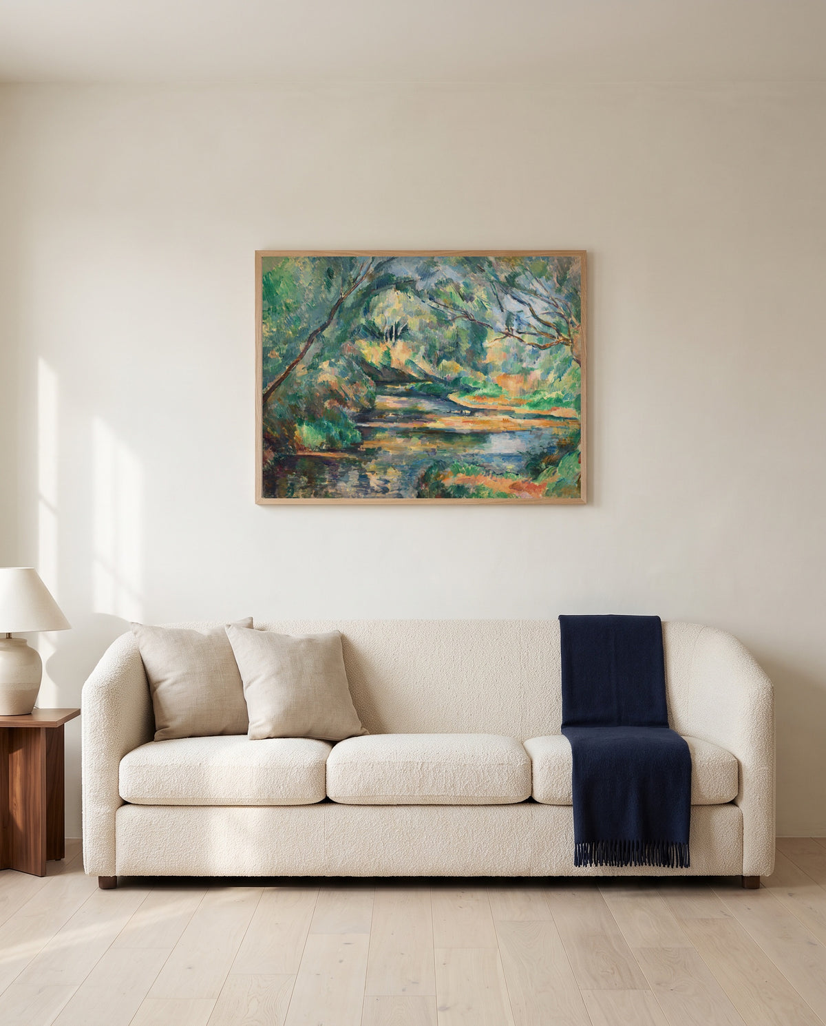 The Brook by Paul Cézanne framed in natural oak above a cream sofa in a warm living room