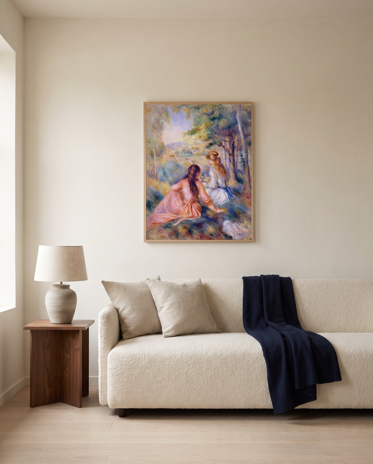 In the Meadow by Pierre-Auguste Renoir framed in natural oak above a cream sofa in a warm living room