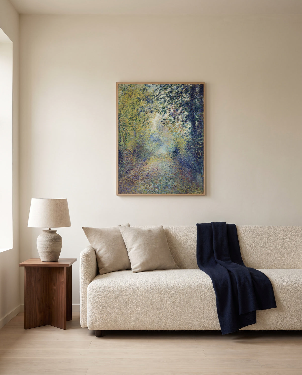 In the Woods by Pierre-Auguste Renoir framed in natural oak above a cream sofa in a warm living room