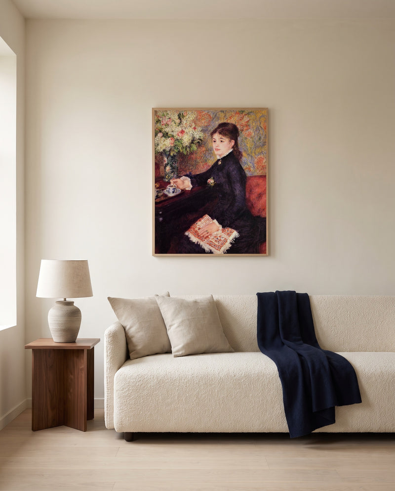 The Cup of Chocolate by Pierre-Auguste Renoir framed in natural oak above a cream sofa in a warm living room