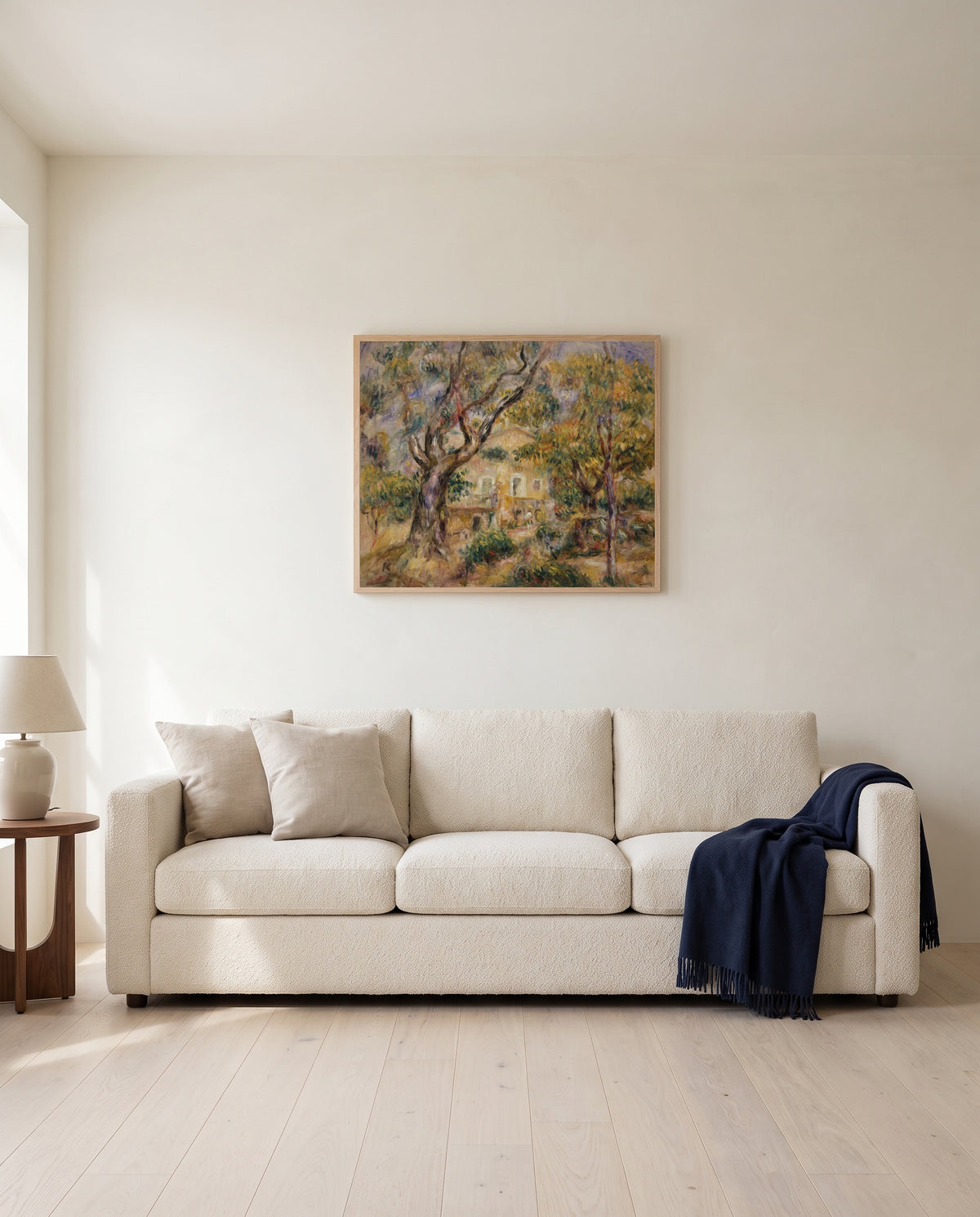 The Farm at Les Collettes by Pierre-Auguste Renoir framed in natural oak above a cream sofa in a warm living room