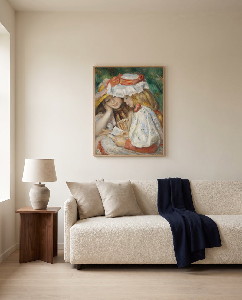 Two Girls Reading by Pierre-Auguste Renoir framed in natural oak above a cream sofa in a warm living room