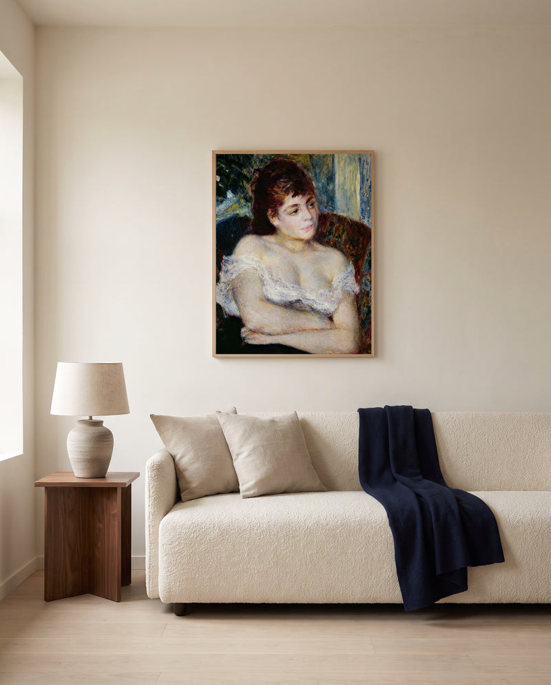 Woman in an Armchair by Pierre-Auguste Renoir framed in natural oak above a cream sofa in a warm living room
