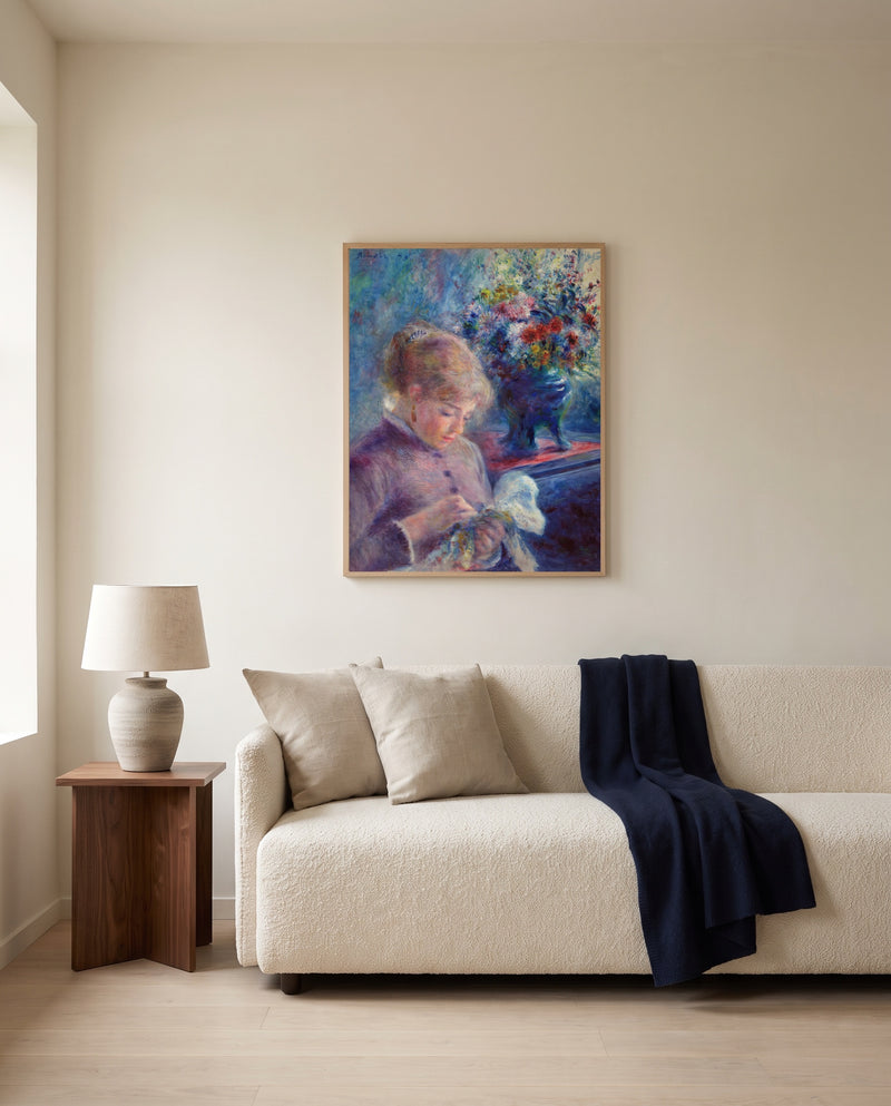 Young Woman Sewing by Pierre-Auguste Renoir framed in natural oak above a cream sofa in a warm living room