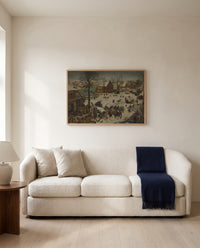 The Census at Bethlehem by Pieter Bruegel the Elder framed in natural oak above a cream sofa in a warm living room