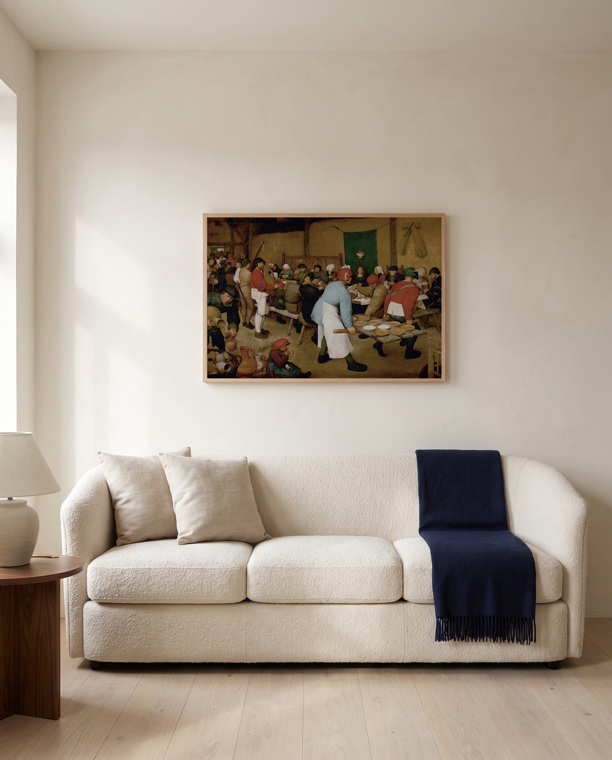 The Peasant Wedding by Pieter Bruegel the Elder framed in natural oak above a cream sofa in a warm living room