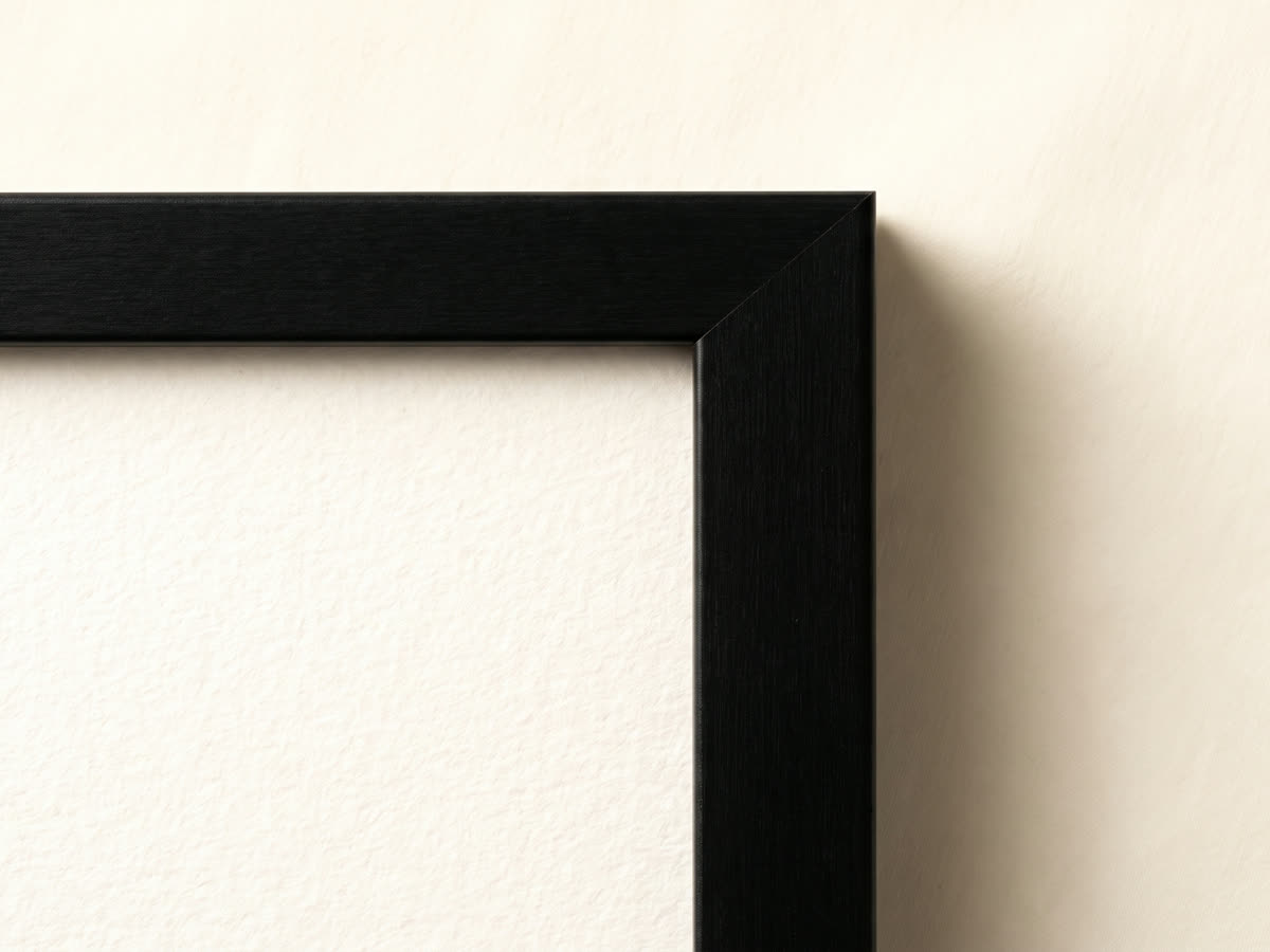 Close view of a black frame corner, showing the bevelled edge and the texture of the fine-art paper behind it.